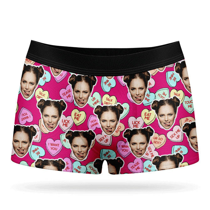 This image displays a pair of custom boxer shorts designed with a vibrant and playful print of love hearts and sweets. The boxers feature a bright pink background, adorned with images of a woman's face and various candies, adding a unique and cheeky touch.