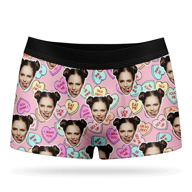 This image displays a pair of custom boxer shorts designed with a vibrant and playful print of love hearts and sweets. The boxers feature a bright pink background, adorned with images of a woman's face and various candies, adding a unique and cheeky touch.
