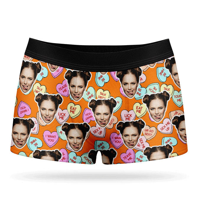 This image displays a pair of custom boxer shorts designed with a vibrant and playful print of love hearts and sweets. The boxers feature a bright pink background, adorned with images of a woman's face and various candies, adding a unique and cheeky touch.